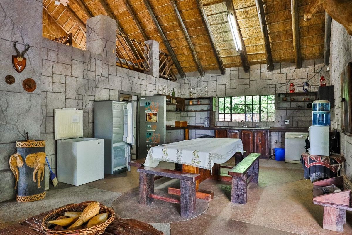 Rustic kitchen area featuring a high thatched roof with exposed timber rafters, stone-clad walls, and functional built-in cabinetry.