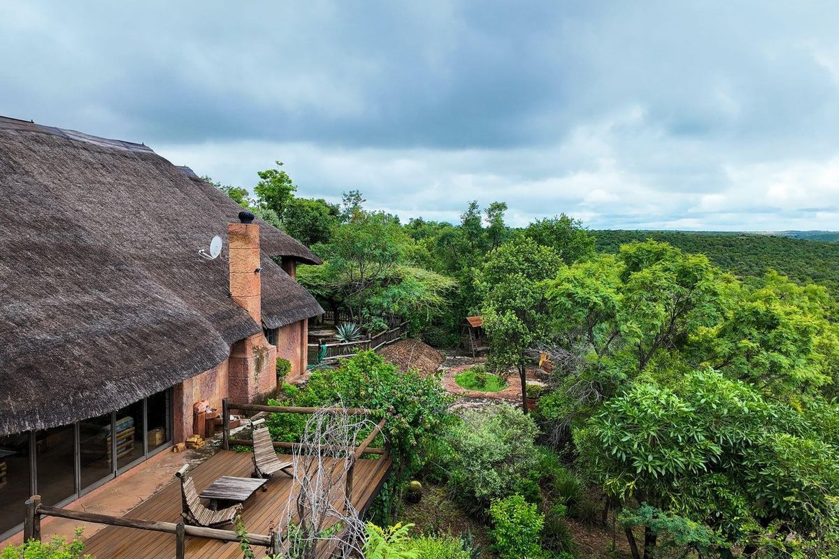 Elevated view of a rustic farmhouse featuring a traditional thatch roof, brick chimney, and a wooden deck overlooking the surrounding natural landscape.