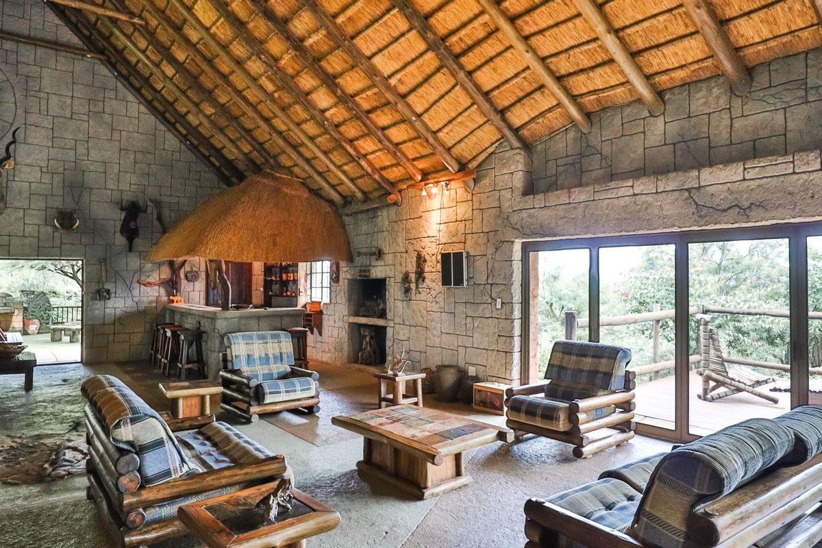 Spacious living area featuring a high thatched roof with exposed timber rafters, stone-clad walls, a built-in fireplace, and a bar, opening onto a timber deck.