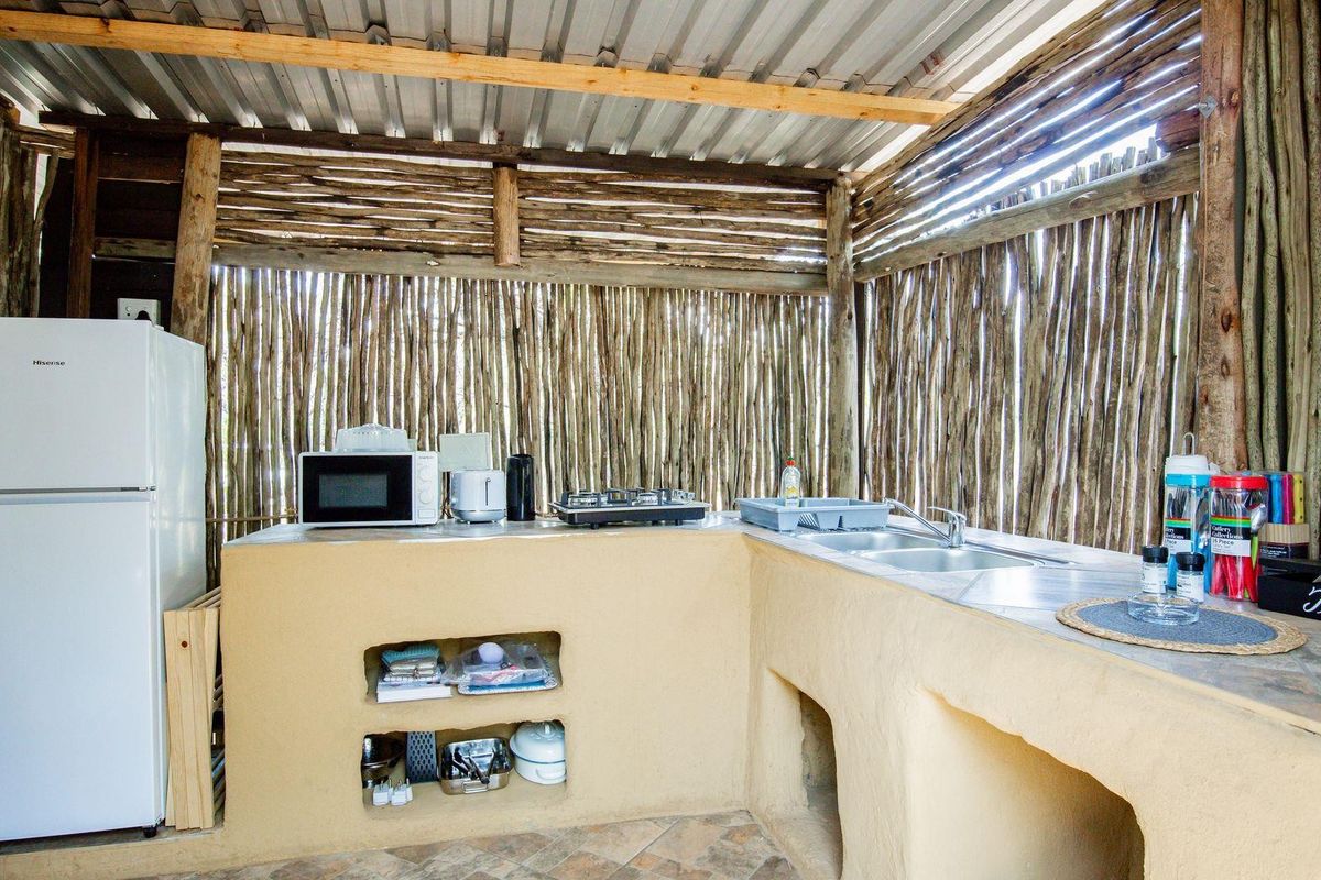 Rustic outdoor kitchen area featuring a built-in masonry counter, stainless steel sink, and corrugated metal roof structure with natural timber wall cladding.