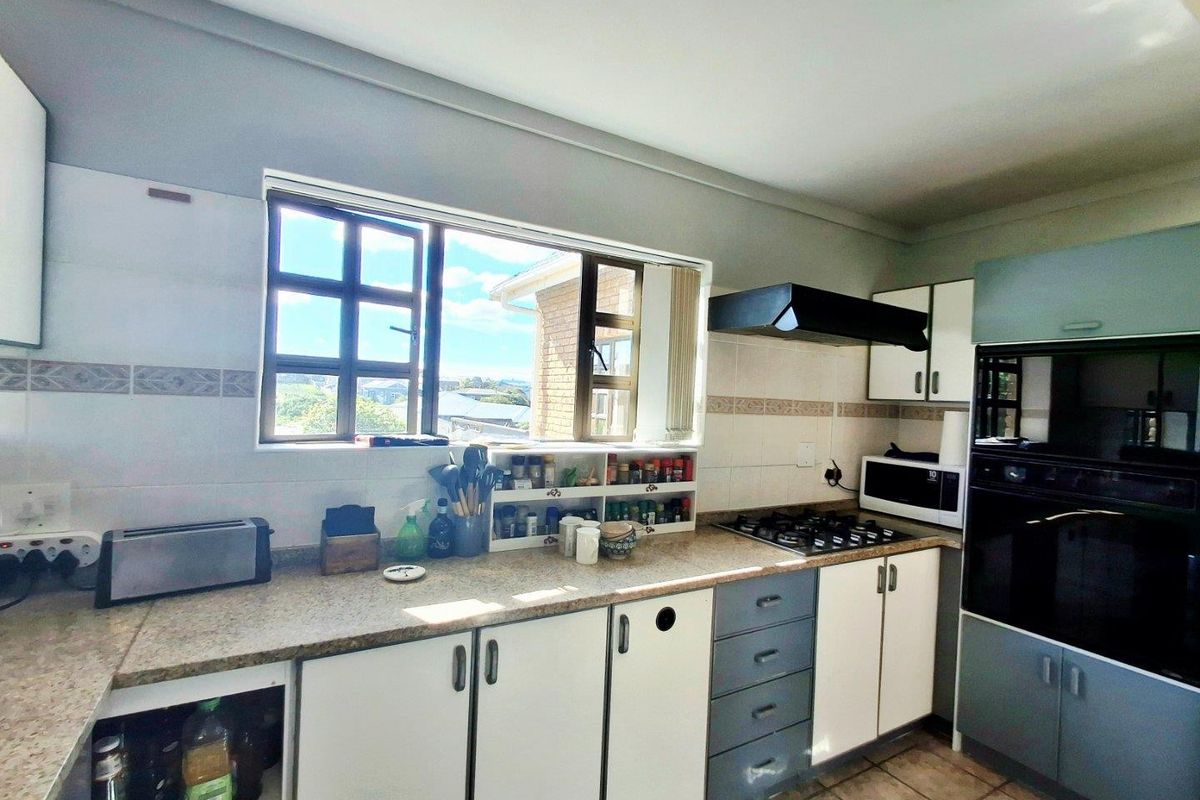 Functional kitchen featuring built-in cabinetry, gas hob, extractor fan, and integrated oven with tiled flooring and ample natural light.