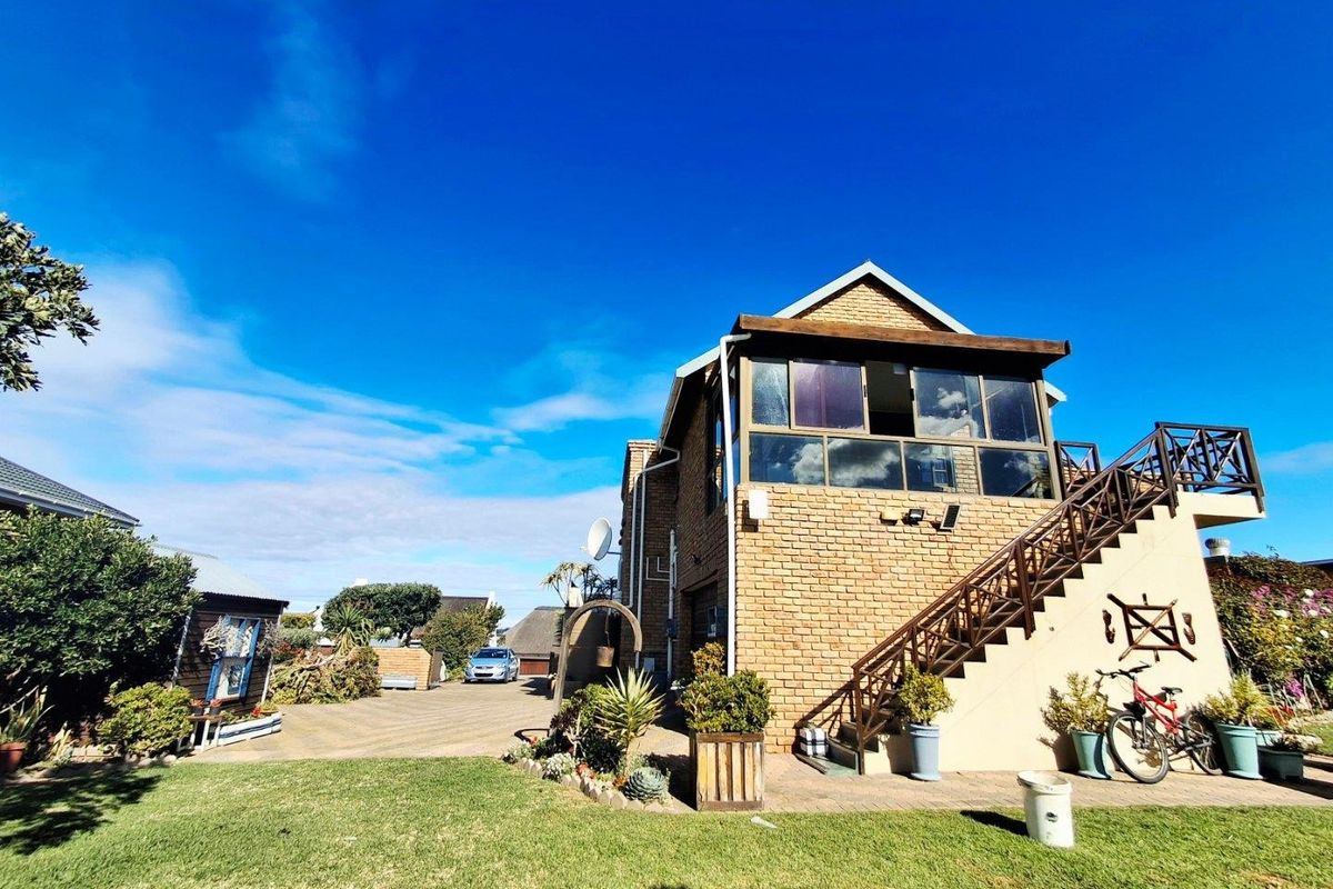 Rear view of a double-story brick house featuring an elevated balcony, external staircase, paved driveway, and a well-maintained garden area.
