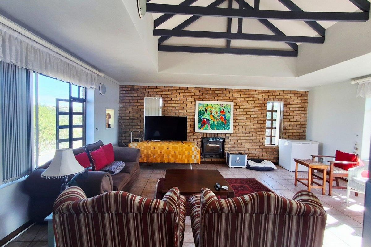 Spacious living room featuring a high vaulted ceiling with exposed beams, a prominent face-brick feature wall, and large windows providing ample natural light.
