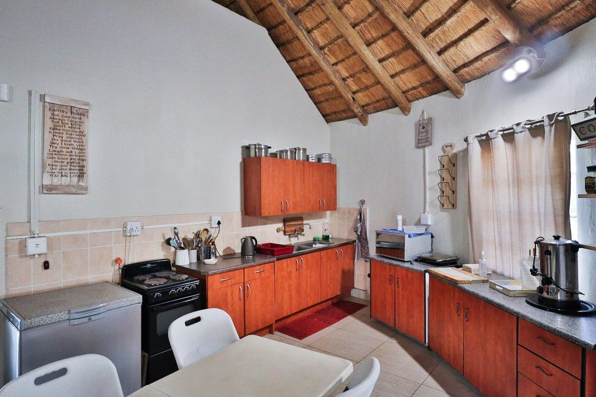A rustic kitchen featuring wooden cabinetry, a tiled backsplash, and a high exposed thatch roof ceiling, providing a traditional farm-style aesthetic.
