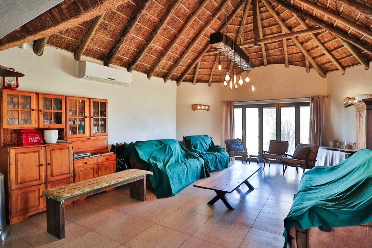 Spacious living area featuring a high vaulted thatched roof, exposed timber beams, tiled flooring, and large glass doors leading to the outdoors.