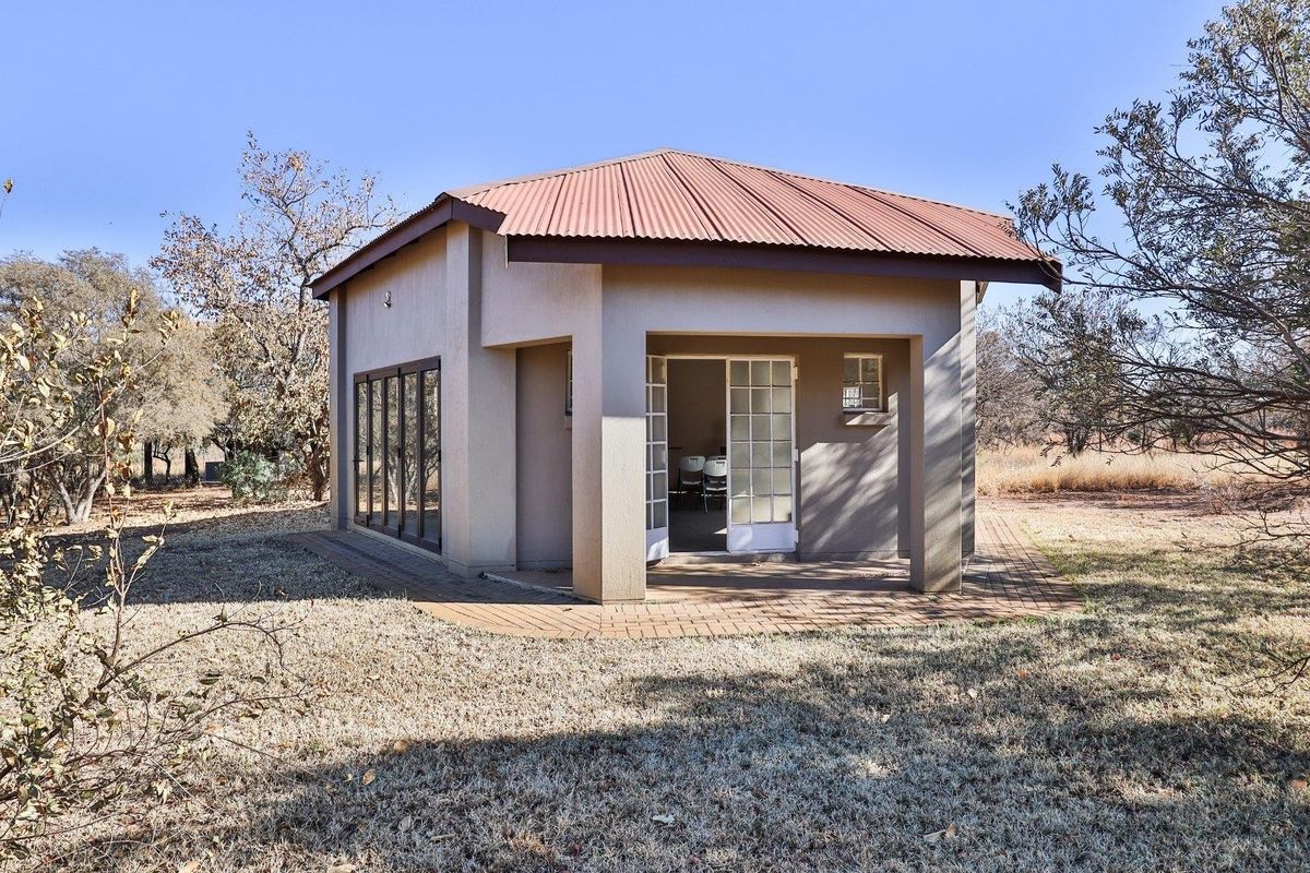A detached outbuilding or cottage featuring a corrugated metal roof, paved patio area, and large glass sliding doors set within a rural farm landscape.
