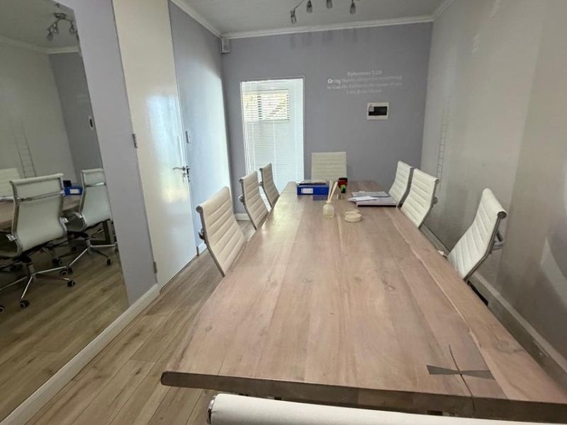 A professional office meeting room featuring wood-look flooring, a large central boardroom table, and a full-length wall mirror.