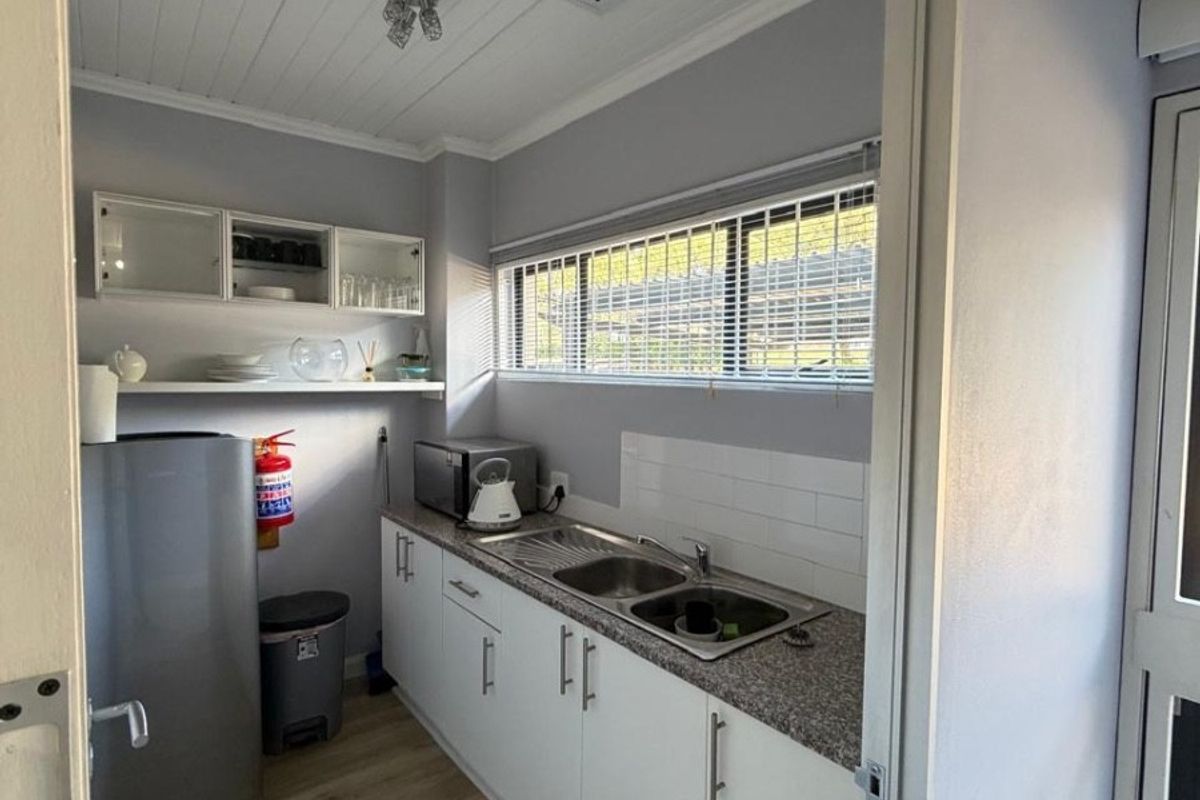 A compact office kitchenette featuring white cabinetry, a double stainless steel sink, granite-style countertops, and wood-look flooring.