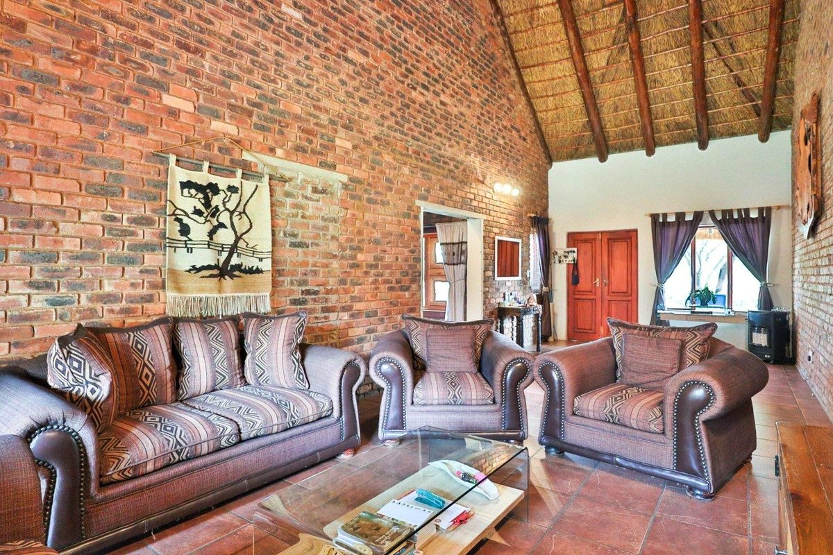 Spacious living room featuring exposed brick walls, high vaulted thatched ceiling with exposed timber beams, and terracotta floor tiles.