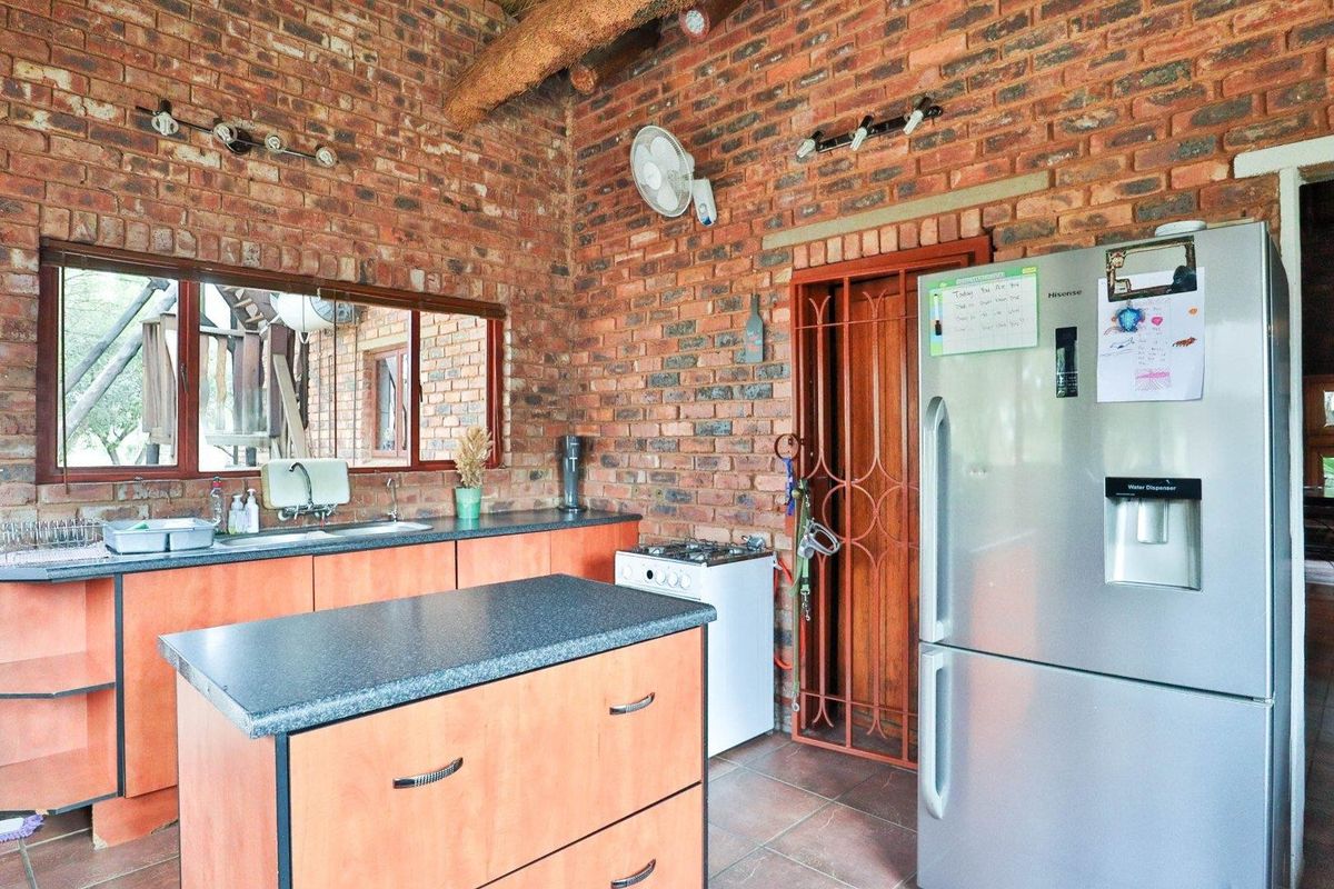 Rustic kitchen featuring exposed brick walls, wooden cabinetry, a central island, and a built-in sink area with large windows overlooking the exterior.