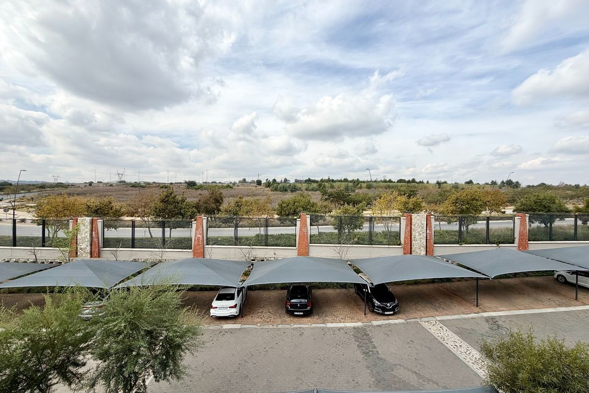 An elevated view of the apartment complex parking area featuring covered shade cloth carports and a secure perimeter wall.
