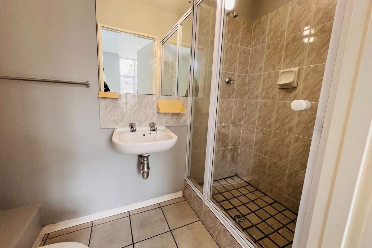 A functional bathroom featuring a wall-mounted basin, a glass-enclosed shower with tiled walls, and neutral floor tiling.