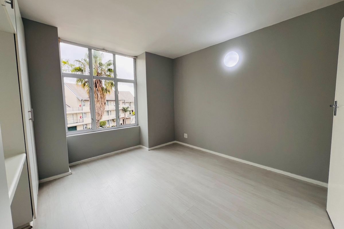 A bright and spacious bedroom featuring neutral grey walls, light laminate flooring, and built-in cupboards, offering a clean and modern blank canvas.