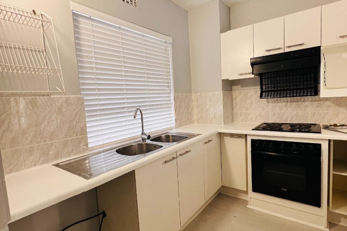 A functional kitchen featuring built-in cabinetry, a stainless steel sink, an integrated oven with hob, and an extractor fan, ready for modernization.