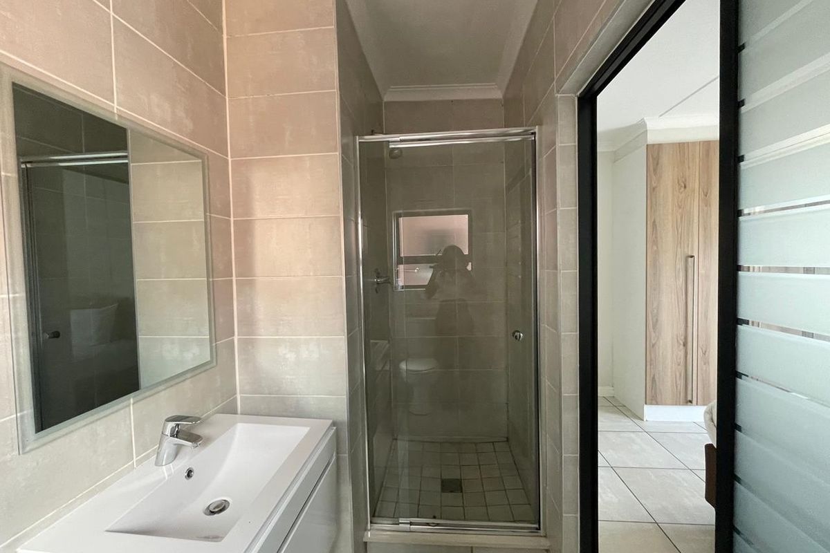 Modern bathroom featuring a glass-enclosed shower, wall-mounted vanity with basin, and neutral floor-to-ceiling tiling, with direct access to the bedroom area.