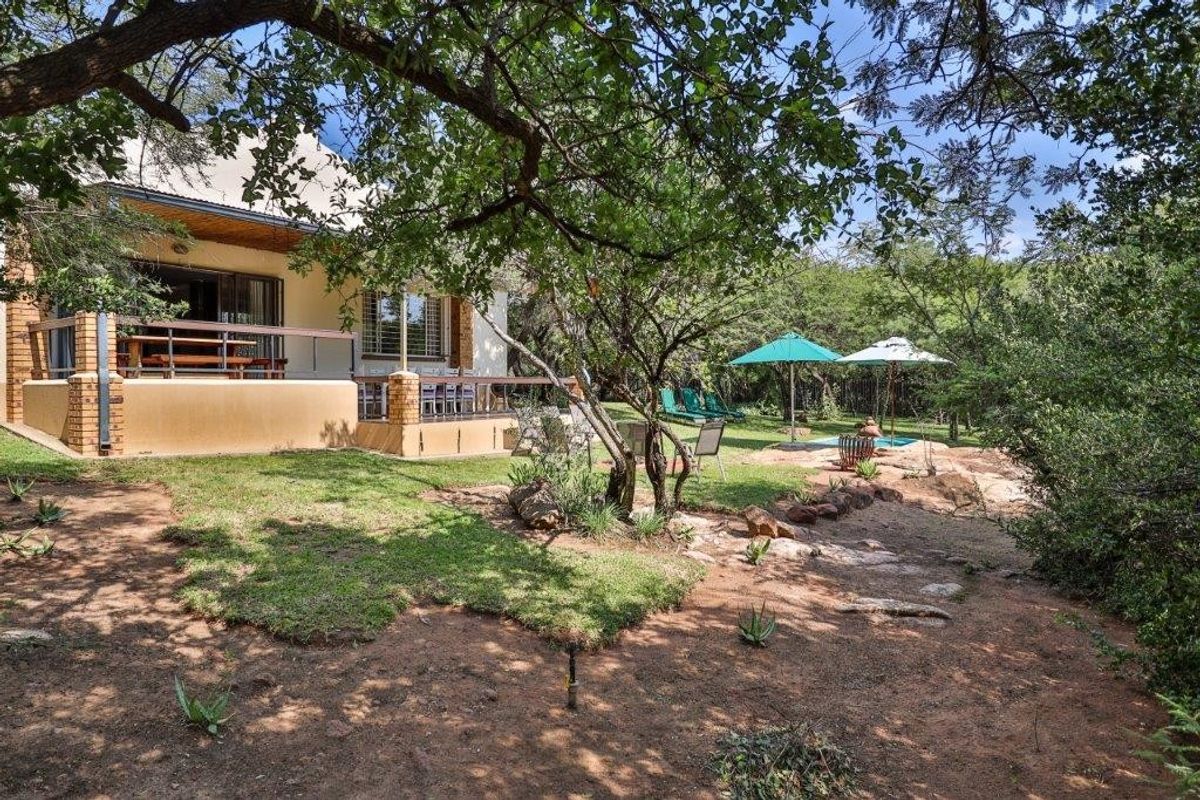 A view of the rear exterior of the farm property, featuring a covered patio, landscaped garden, and natural rocky terrain.