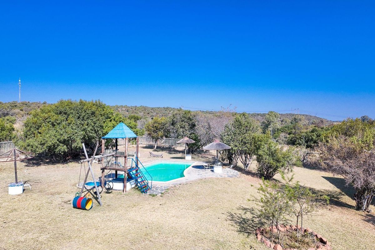 Outdoor pool area featuring a swimming pool with stone decking, thatched umbrellas, and a children's playground structure set within a spacious garden.