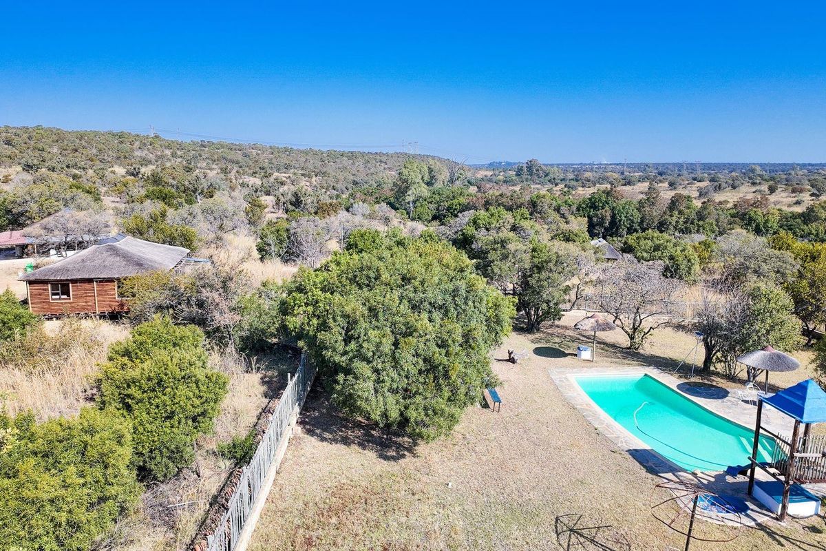 Aerial view of a farm property featuring a swimming pool, a thatched roof cabin, and expansive natural landscape.