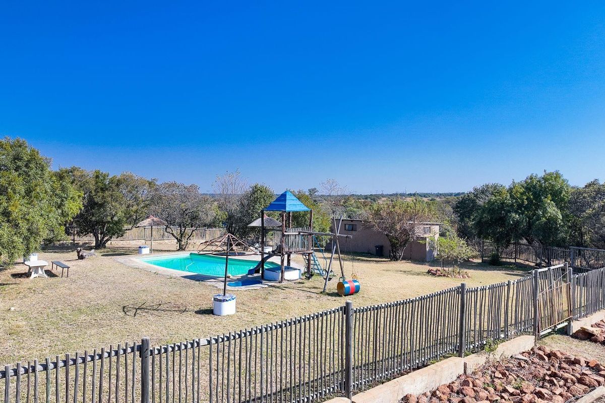 Outdoor pool area featuring a swimming pool, concrete surround, and metal perimeter fencing set within a spacious garden landscape.
