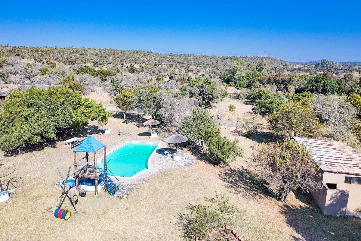 Aerial view of a farm property featuring a swimming pool with stone patio and a detached outbuilding set within a large natural landscape.
