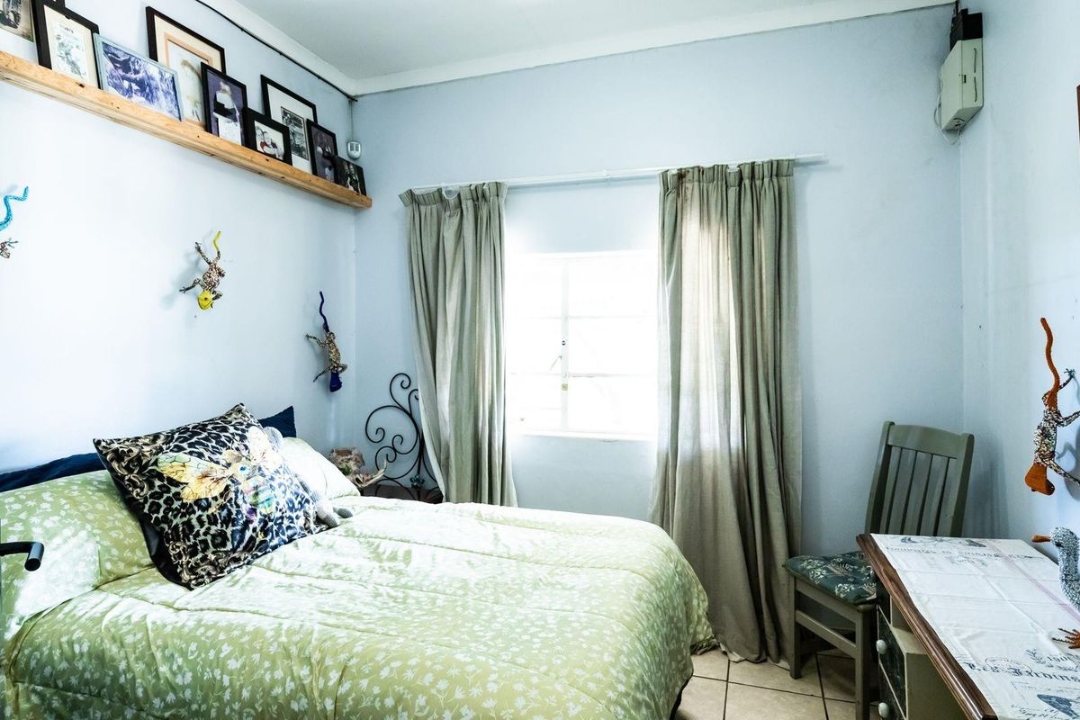 A functional bedroom featuring tiled flooring, a window with curtain tracks, and a built-in wooden display shelf.