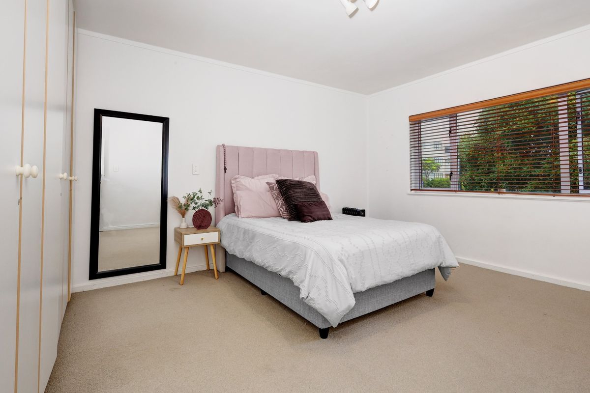 A well-lit bedroom featuring neutral carpeting, built-in wardrobe storage, and large windows with fitted blinds.