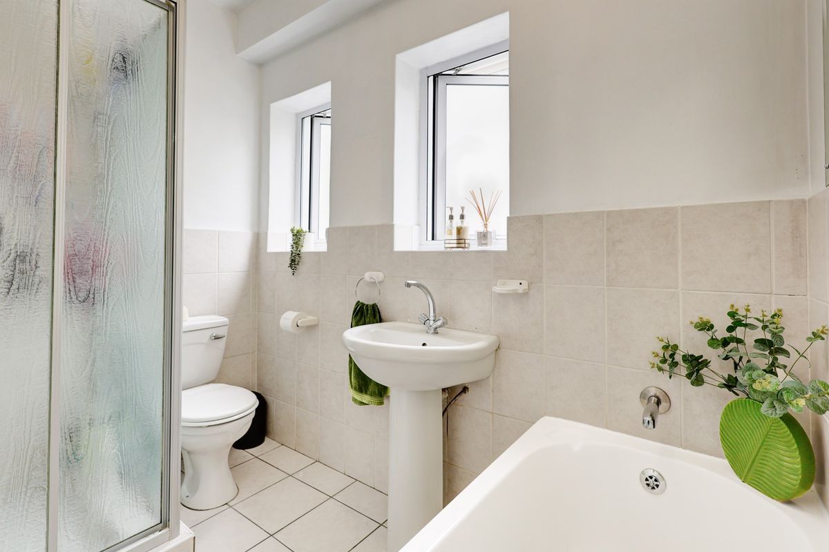 A functional bathroom featuring a pedestal sink, a standard toilet, and a shower enclosure with tiled walls and flooring.