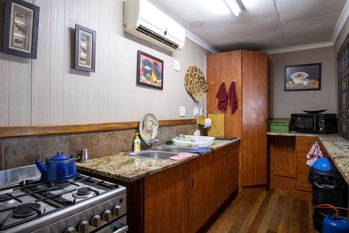 A functional kitchen featuring granite countertops, wooden cabinetry, a gas stove, and a wall-mounted air conditioning unit.