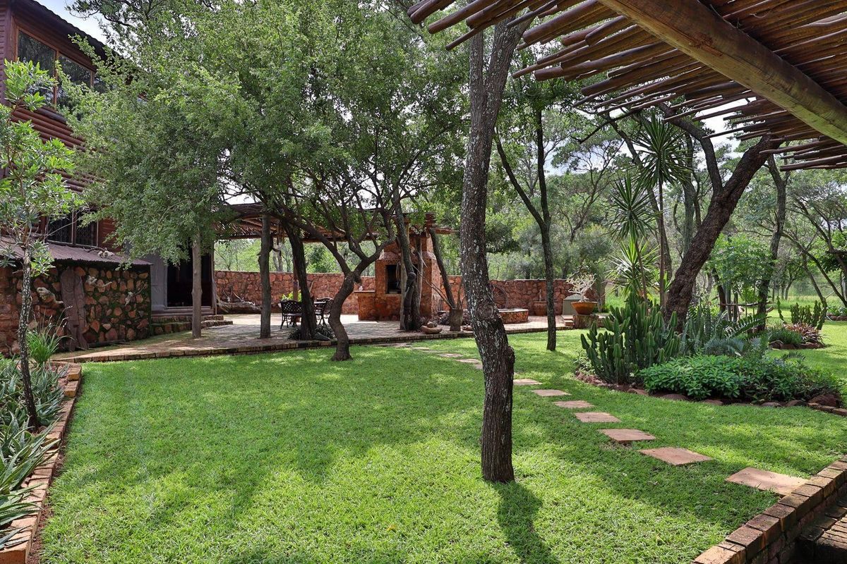 Spacious rear garden featuring a paved patio area with a built-in stone braai, wooden pergola structure, and established landscaping.