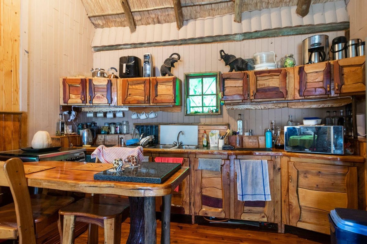 Rustic farm-style kitchen featuring custom timber cabinetry, exposed thatch ceiling, wooden wall paneling, and a built-in breakfast nook.