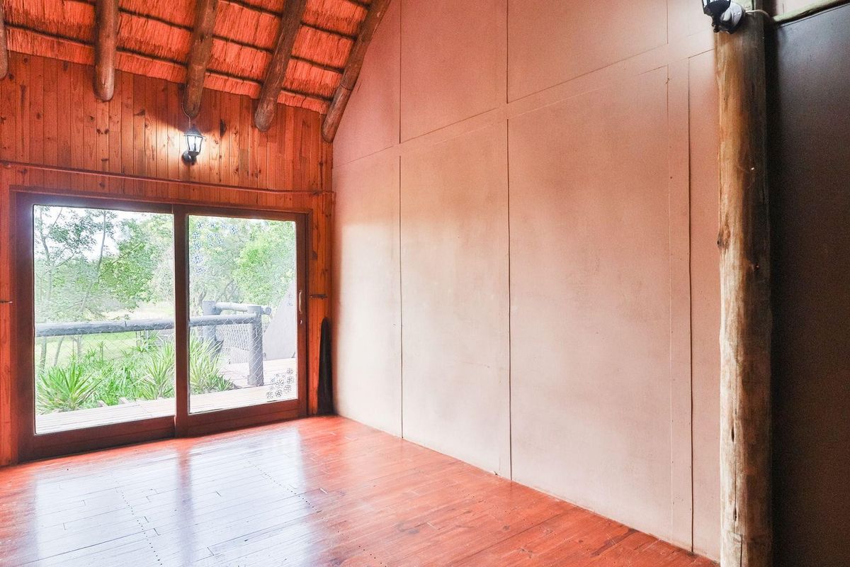 Spacious living area featuring a high thatched roof, exposed timber beams, wooden flooring, and large sliding glass doors opening to an outdoor deck.