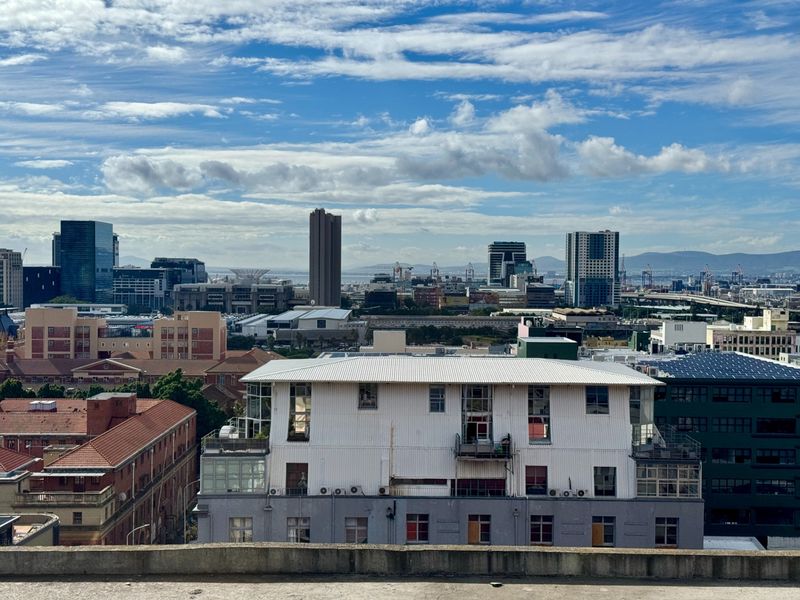 An elevated urban cityscape view showcasing surrounding buildings and the city skyline under a partly cloudy sky.