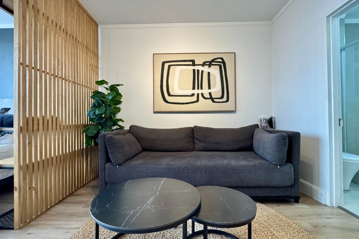 A modern living area featuring light wood flooring, a decorative timber slat room divider, and access to an adjacent bathroom.