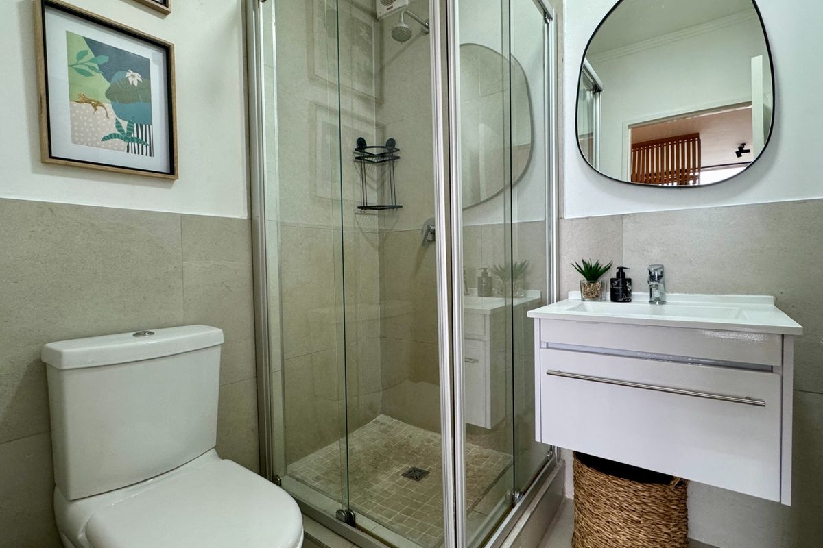 A compact, modern bathroom featuring a glass-enclosed shower, a wall-mounted vanity with basin, and a standard toilet with neutral wall tiling.
