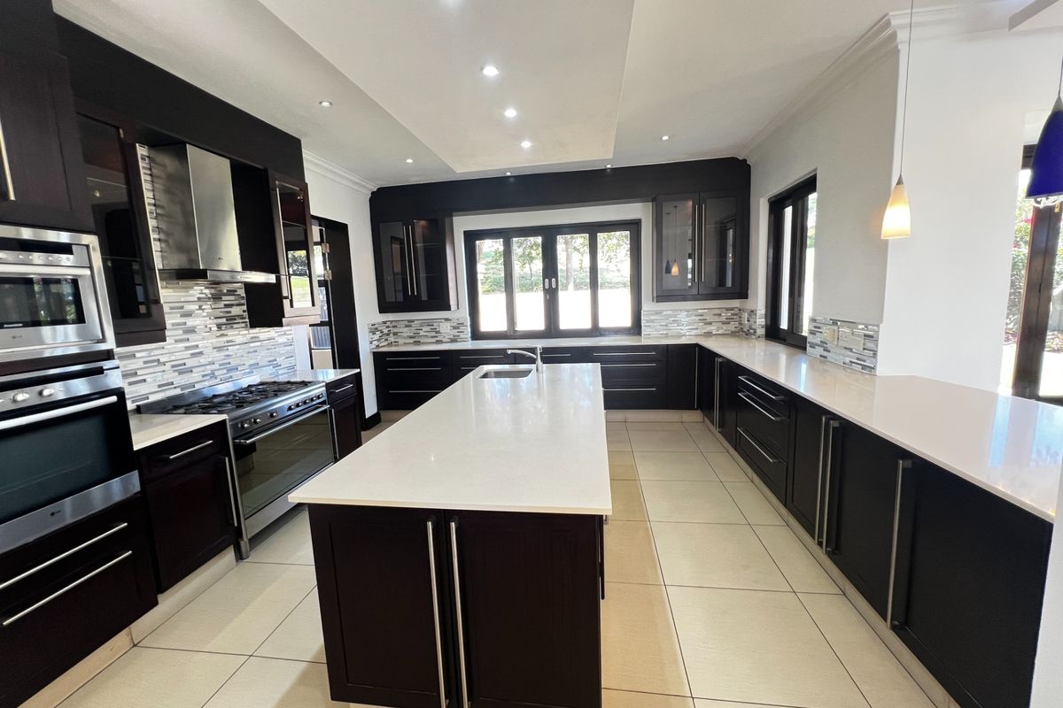 Modern kitchen featuring dark cabinetry, a large central island with a sink, stone countertops, and built-in stainless steel appliances.