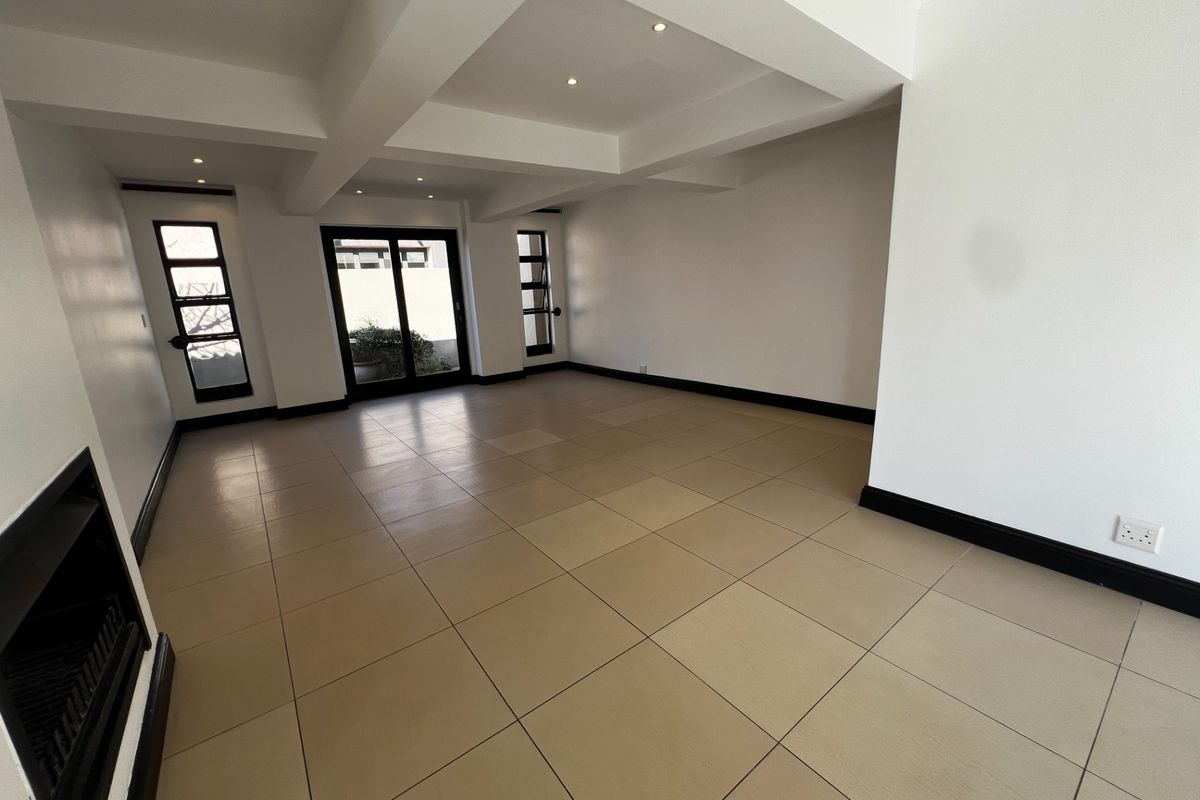 A spacious, empty living area featuring large ceramic floor tiles, recessed ceiling lighting, and a built-in fireplace with black trim.