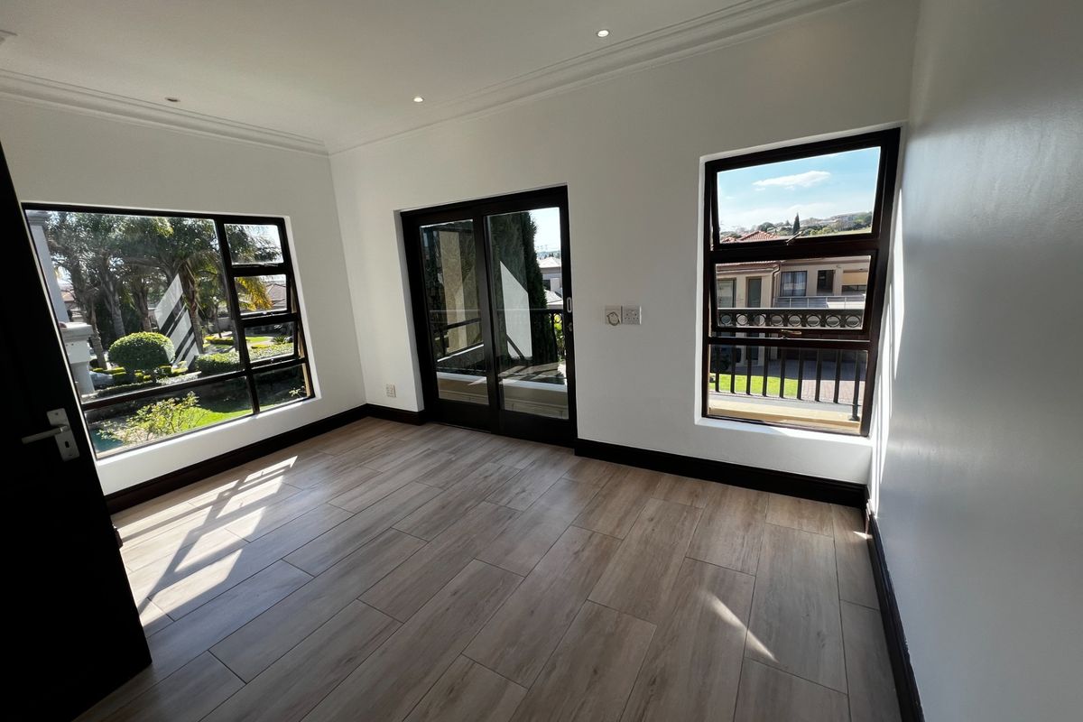 A bright, empty bedroom featuring modern wood-look tile flooring, recessed ceiling lighting, and large windows providing natural light and views.