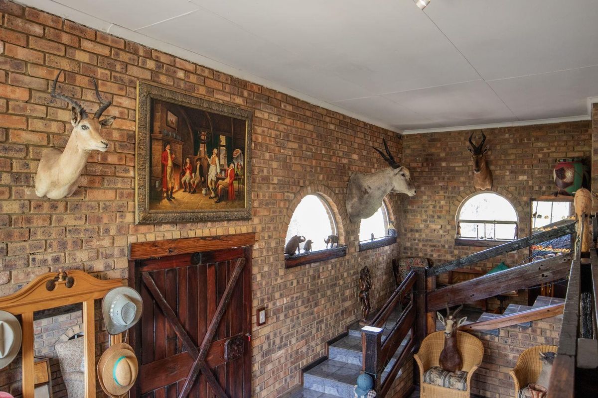 Interior view of a rustic farm-style living area featuring exposed face-brick walls, arched windows, and a wooden staircase with a timber balustrade.