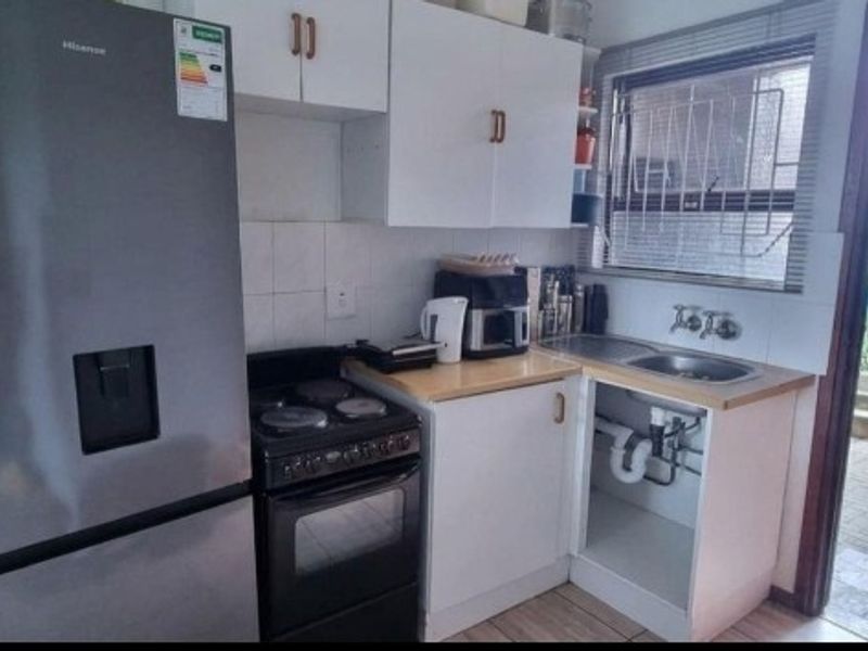 Compact kitchen featuring built-in cabinetry, a stainless steel sink, and a freestanding stove, with direct access to the exterior patio area.