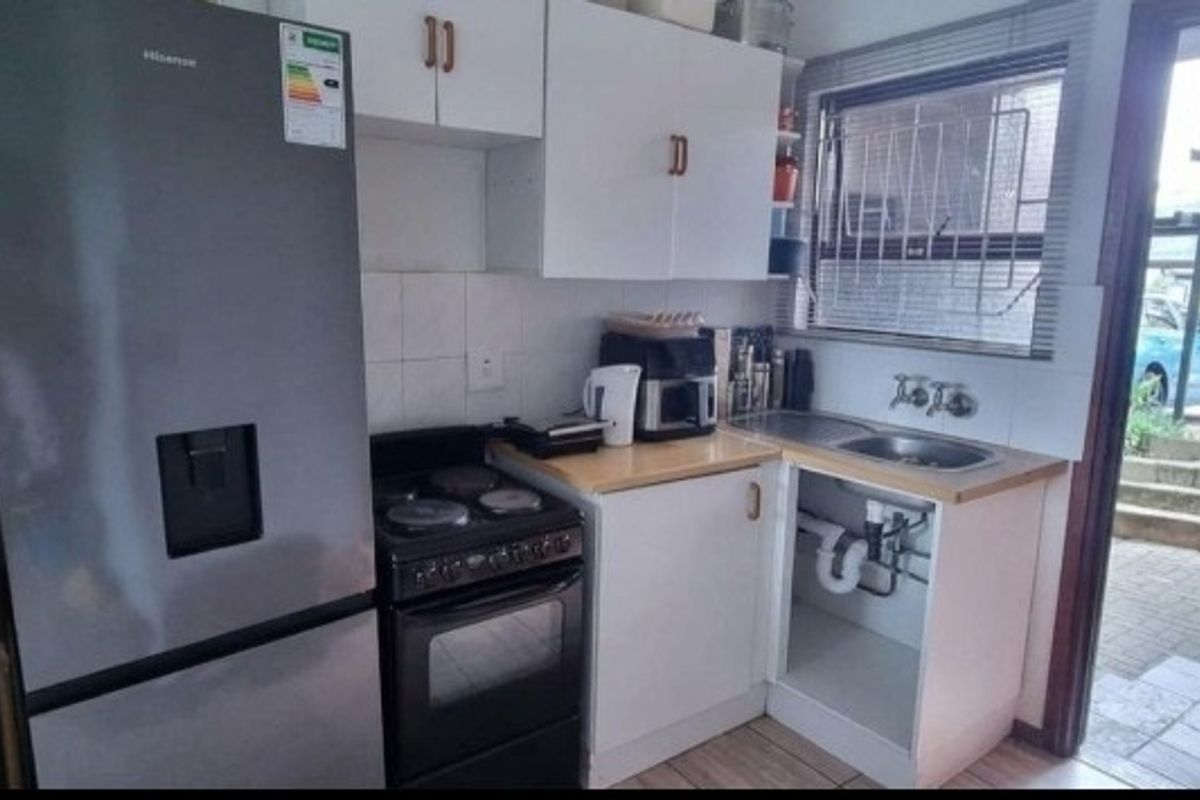 Compact kitchen featuring built-in cabinetry, a stainless steel sink, and a freestanding stove, with direct access to the exterior patio area.