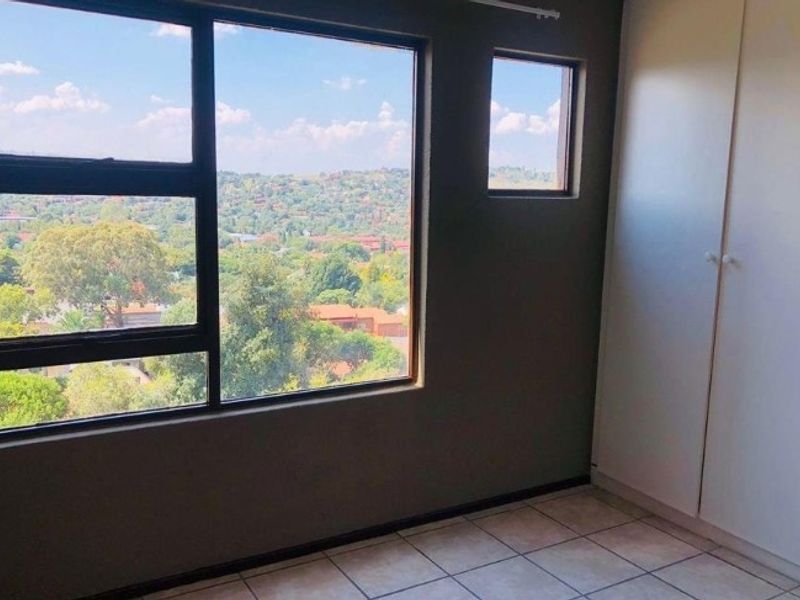 A bedroom featuring tiled flooring, built-in cupboards, and large windows offering an elevated view of the surrounding landscape.