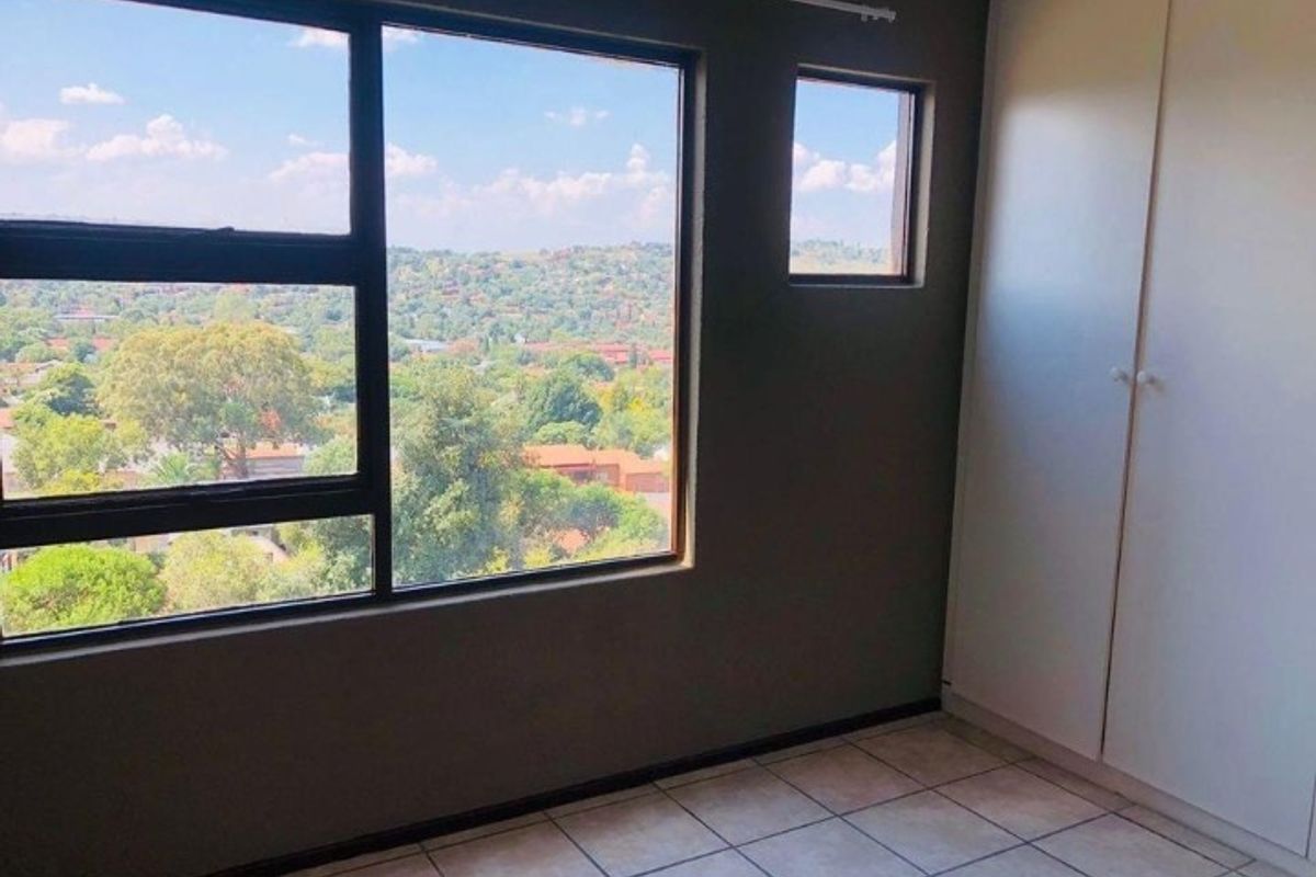 A bedroom featuring tiled flooring, built-in cupboards, and large windows offering an elevated view of the surrounding landscape.