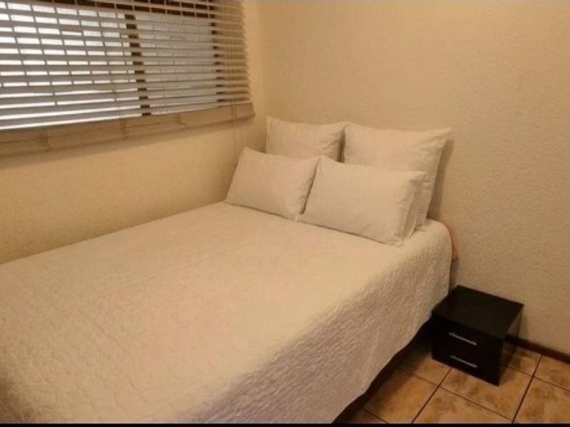 A compact bedroom featuring tiled flooring, textured walls, and horizontal window blinds.