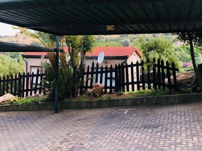 A covered carport area with paved driveway, featuring a garden border and a view of the adjacent property.