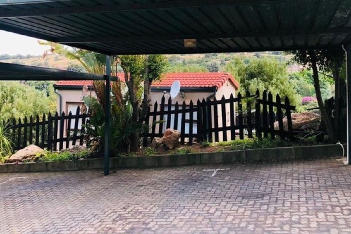 A covered carport area with paved driveway, featuring a garden border and a view of the adjacent property.
