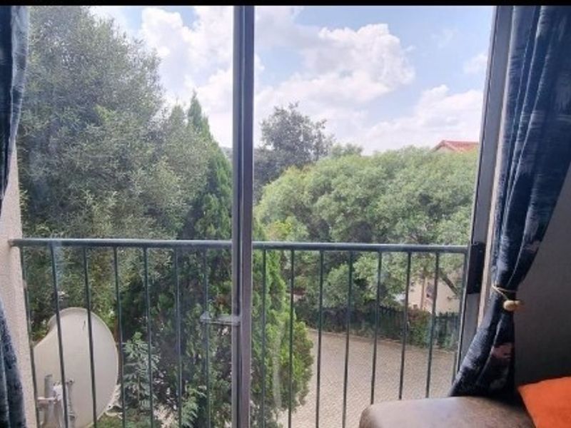 A view from an interior space looking out through a sliding glass door onto a balcony with metal railings and surrounding greenery.