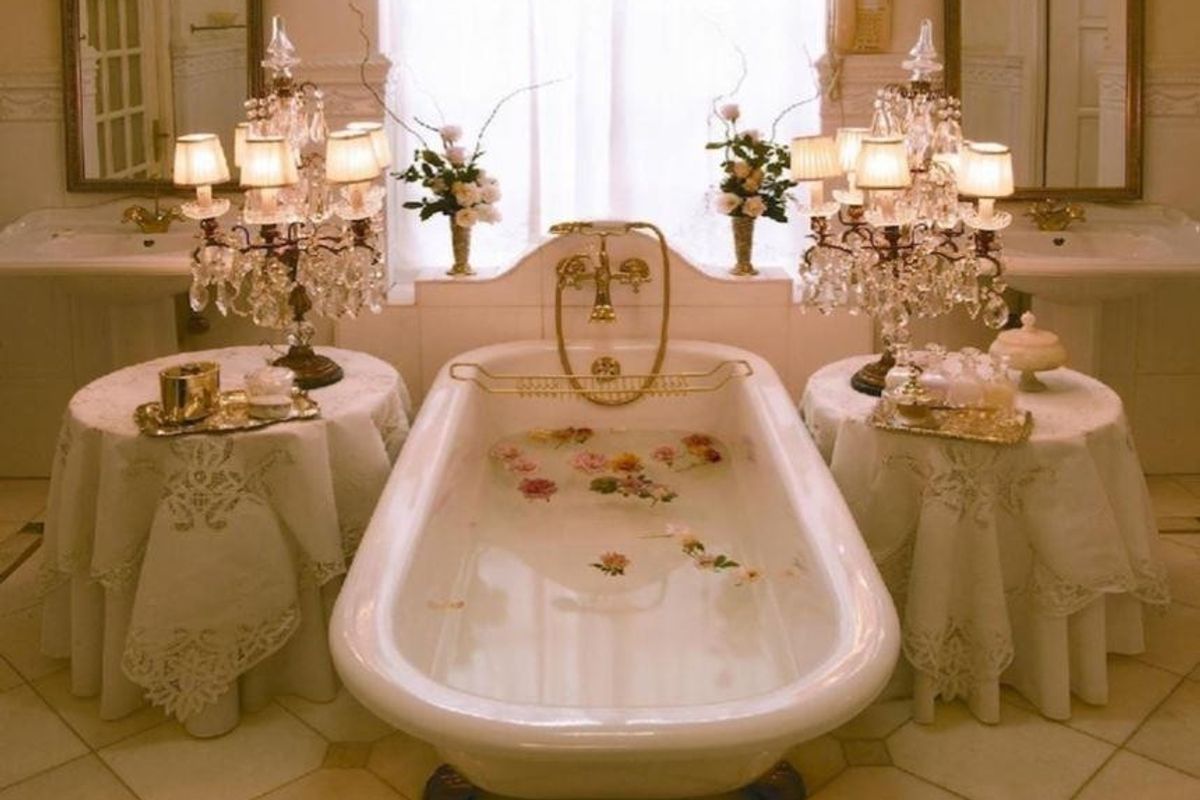 A classic bathroom featuring a central freestanding bathtub, dual pedestal sinks, and elegant brass fixtures, creating a traditional and refined aesthetic.
