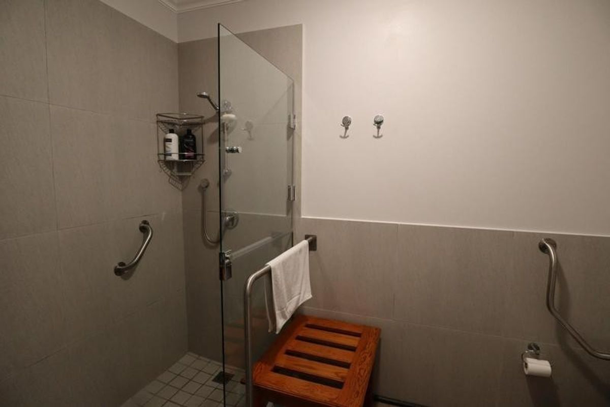 Modern accessible bathroom featuring a walk-in shower with glass screen, grab rails, and neutral wall tiling.