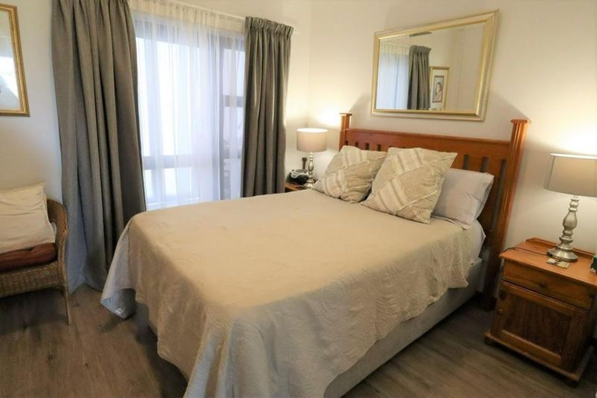 A well-maintained bedroom featuring wood-look flooring, large window with curtain tracks, and neutral wall finishes.