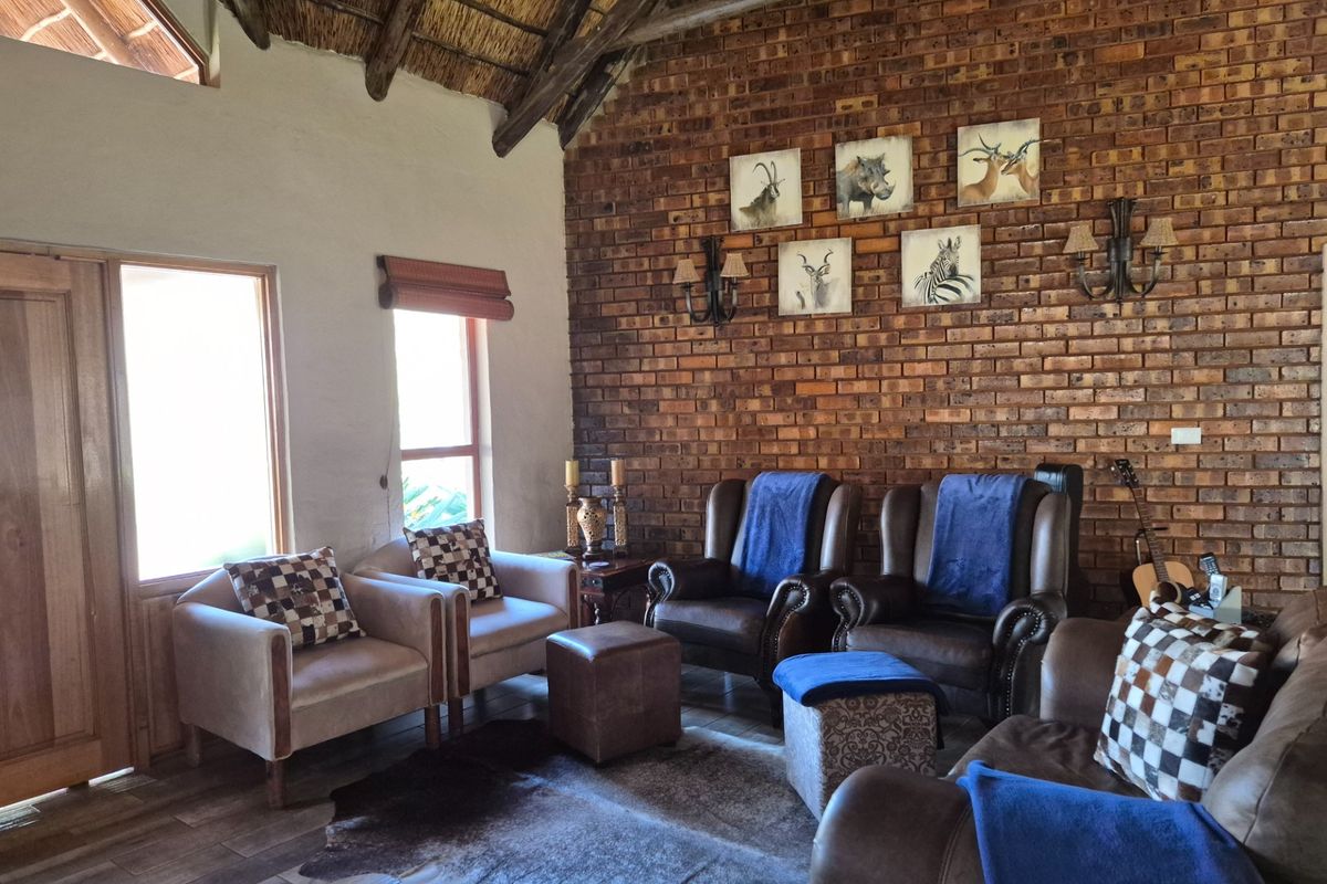 A rustic living room featuring an exposed brick feature wall, high vaulted thatched ceiling with timber beams, and tiled flooring.